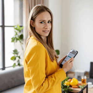 A woman in a yellow blazer standing at a large window with a smartphone in her hands is browsing an 89md73nr09ydjog2c9x5 2
